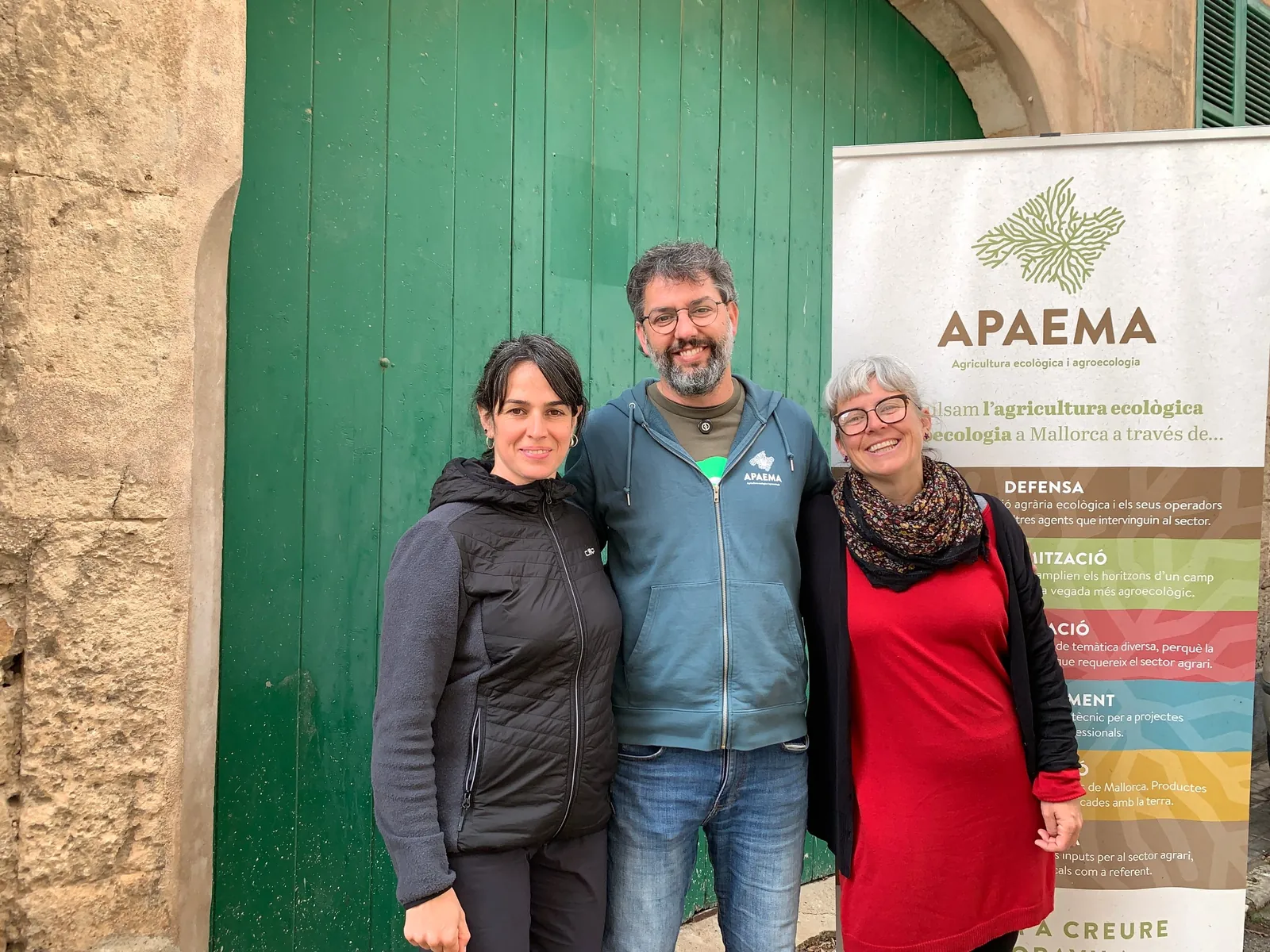 Tres personas junto al cartel de APAEMA frente a una puerta verde