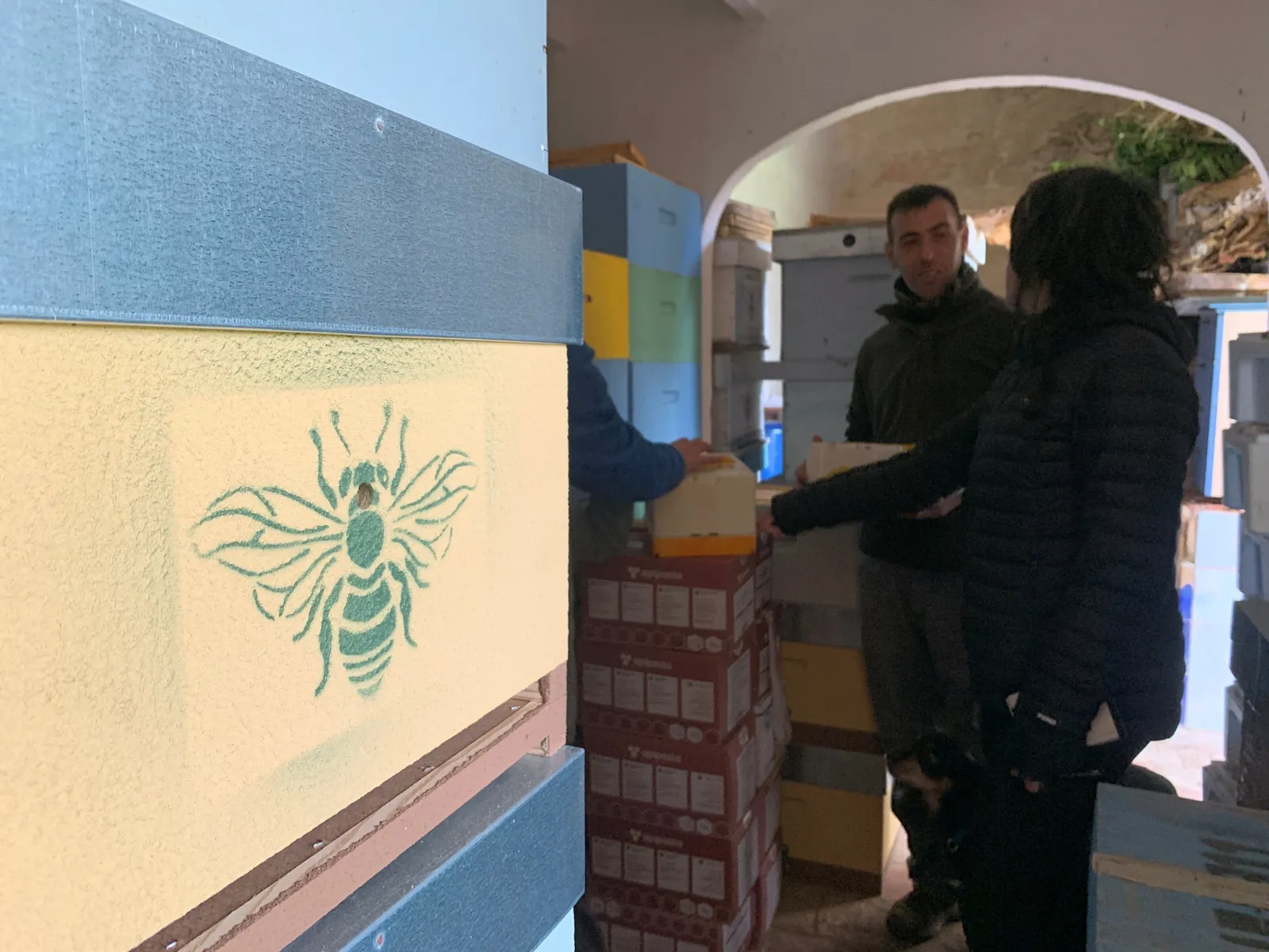 Colmena con una abeja estarcida y dos personas al fondo